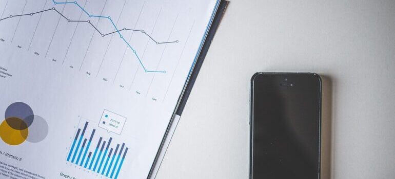 A cellphone on a white table next to papers with graphs.