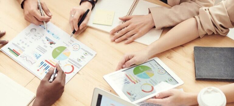 People around a table looking at papers with infographs and pie charts.