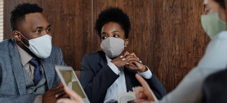 A group of people wearing facemasks talking around a table.