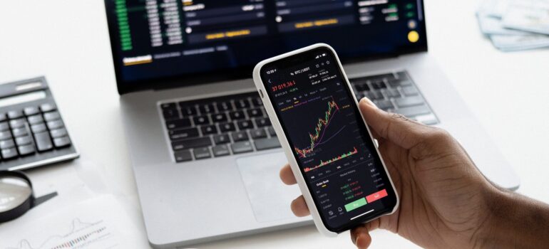 A person using a phone and a laptop to access the same financial data.