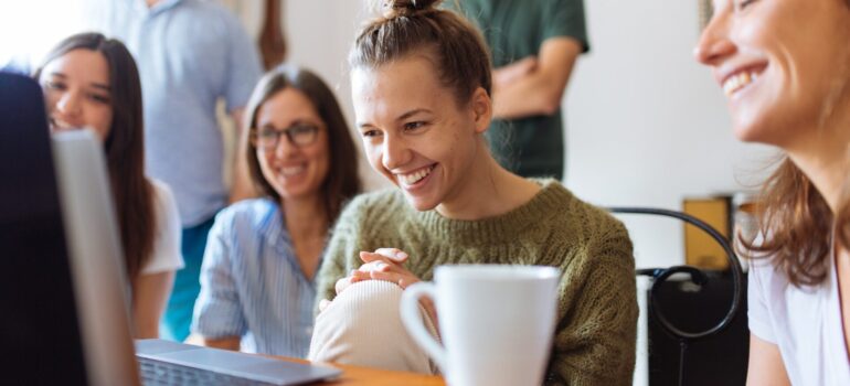 A group of people happily looking at a laptop, showing that periodical surprises can be one of the best customer retention strategies.