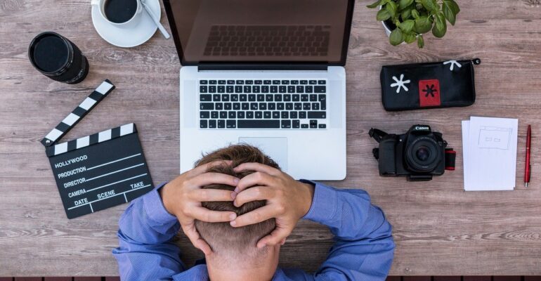 An employee holding his head in a nervous way in front of a laptop.