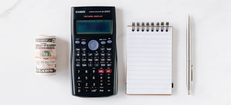 A bundle of money, a calculator, a notebook and a pen.