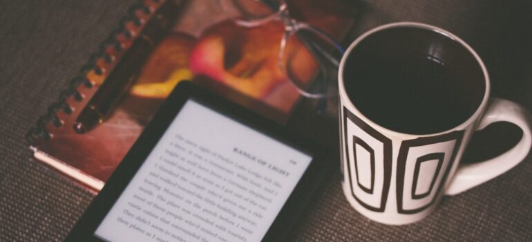 An e-book reader next to a cup of coffee.