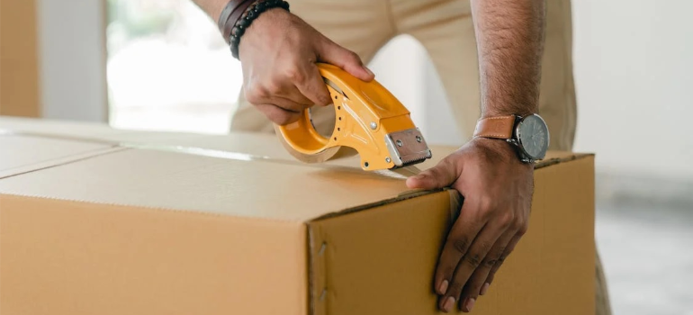 A close-up of a person tapping a moving box with scotch.