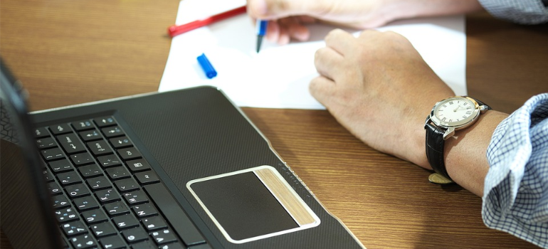 A close-up of a person keeping notes next to a laptop.