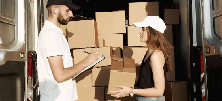A man and a woman sorting through moving boxes stacked in a white van.