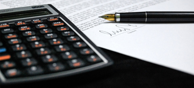 A close-up of a black calculator and pen on a contract.