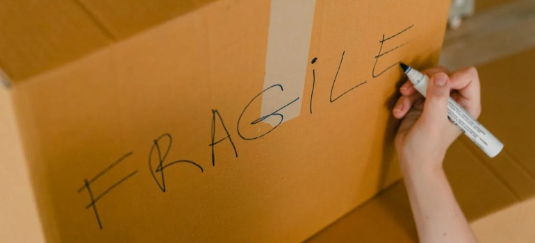 A close-up of a person writing “fragile” on the side of a moving box with a sharpie.