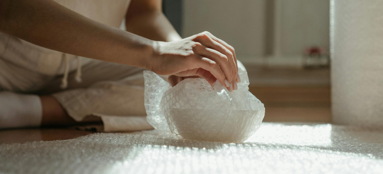 A close-up of hands wrapping up a fragile item with bubble wrap. 